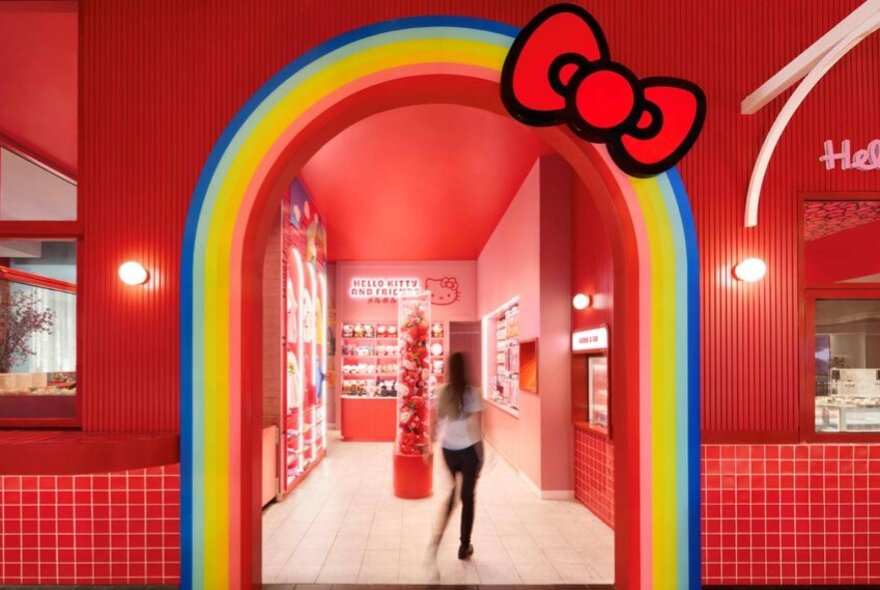 The rainbow entrance to a red shopfront; a woman walking into the store.