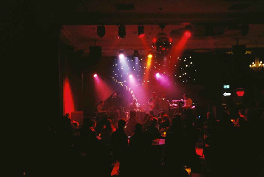 A band playing live music on stage at a club in front of an audience, with red spotlights illuminating the stage.