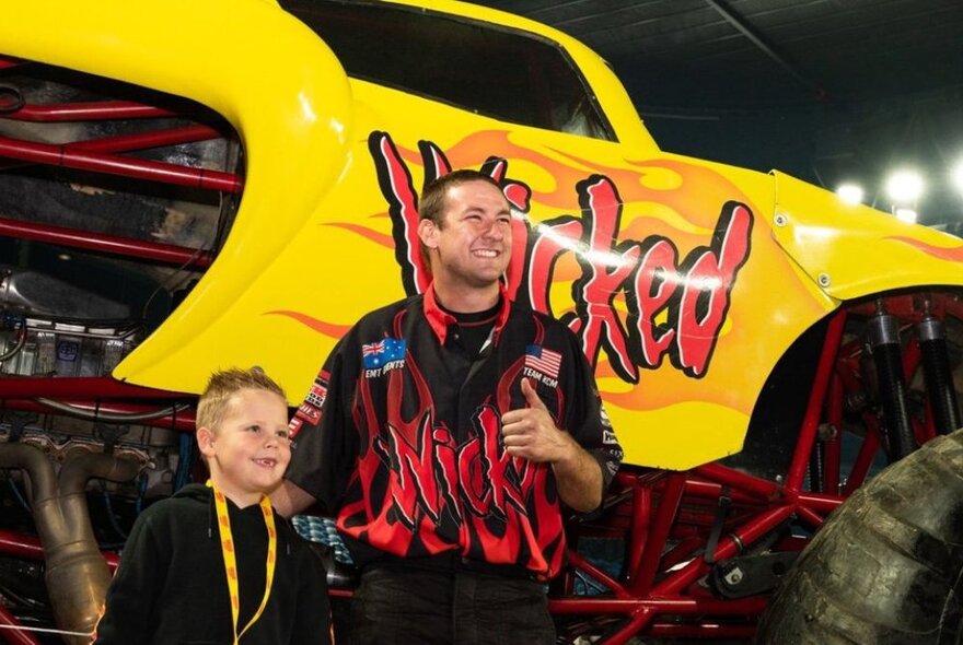 A young boy posing with a man in front of a yellow monster truck. 