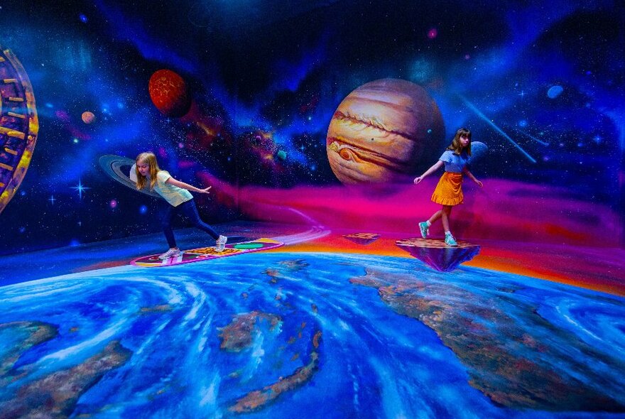 Two children standing in front of a mural painted as outer space