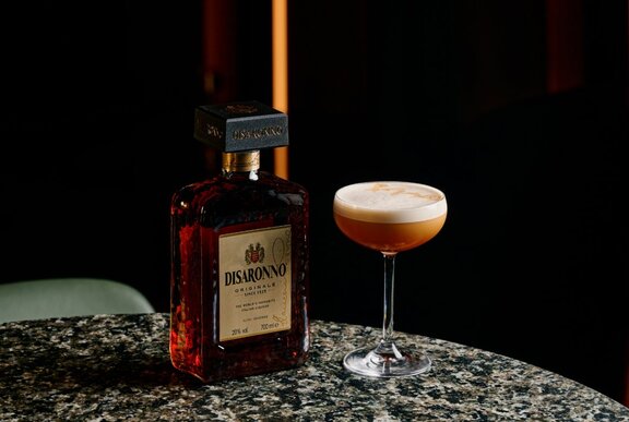 Creamy cocktail next to a bottle of Disaronno on a marble tabletop.