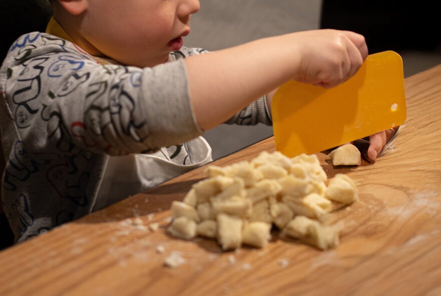 A child slicing gnocchi dough with a yellow slicer.