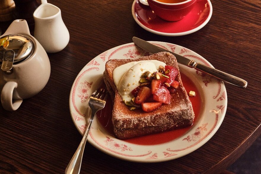 A plate of French toast with strawberries and ice cream, with teapot and teacup.