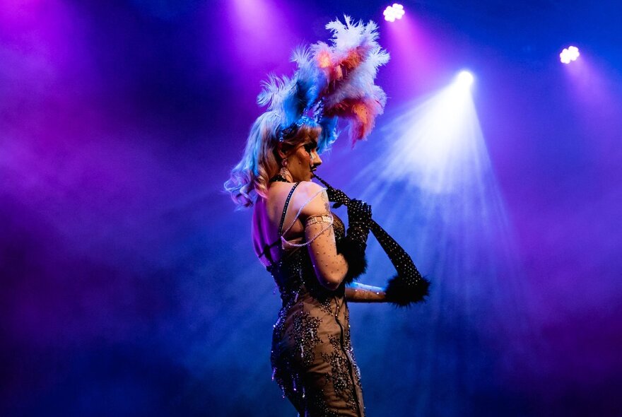 The back view of a burlesque dancer performing on stage in a feathered headdress. 