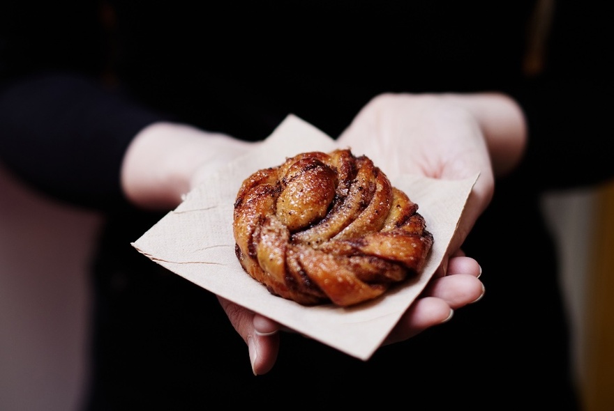 Pastry on serviette, held in two palms against black clothing of bearer.