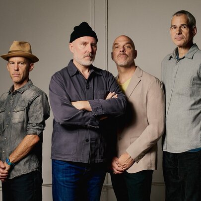 The four band members of The Bad Plus posing in a serious way in a beige toned room. 