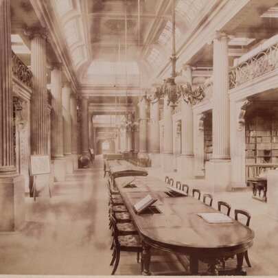A sepia-toned photograph of the interior of a grand, classical-style library hall with a high ceiling and massive fluted columns lining both sides.