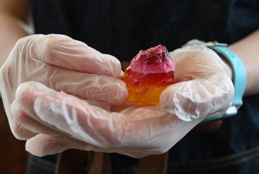 Hands wearing white plastic gloves holding a red blob of resin.