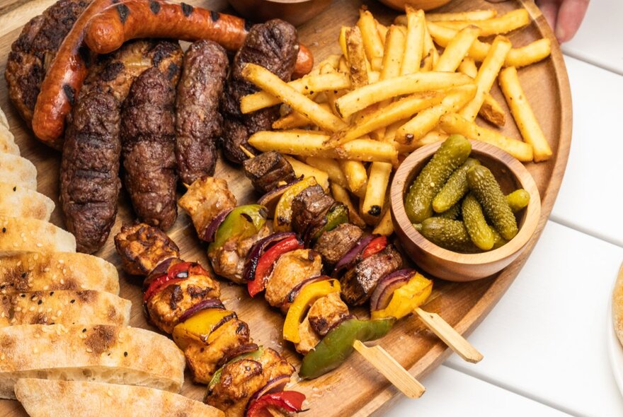 Platter of kebabs and sausages with chips and pickles.