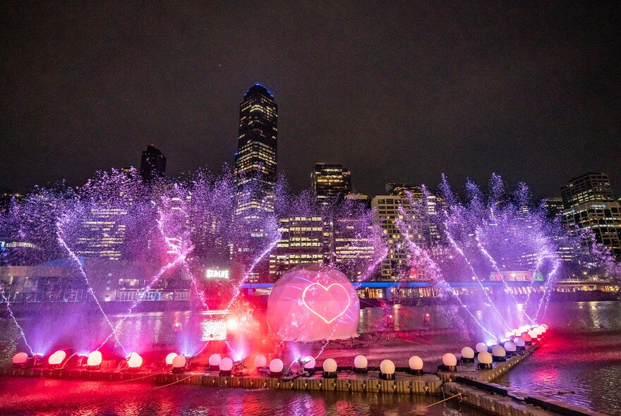 A glowing river show lit up at night with water fountains coming out of it