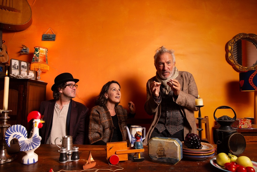 Two musicians and a man with a book in an orange room.