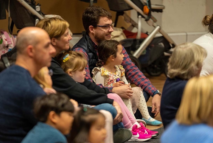 Children seated on parents' knees in rows in an auditorium.