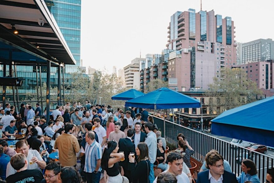 A very crowded rooftop bar in Melbourne with blue shade umbrellas. 