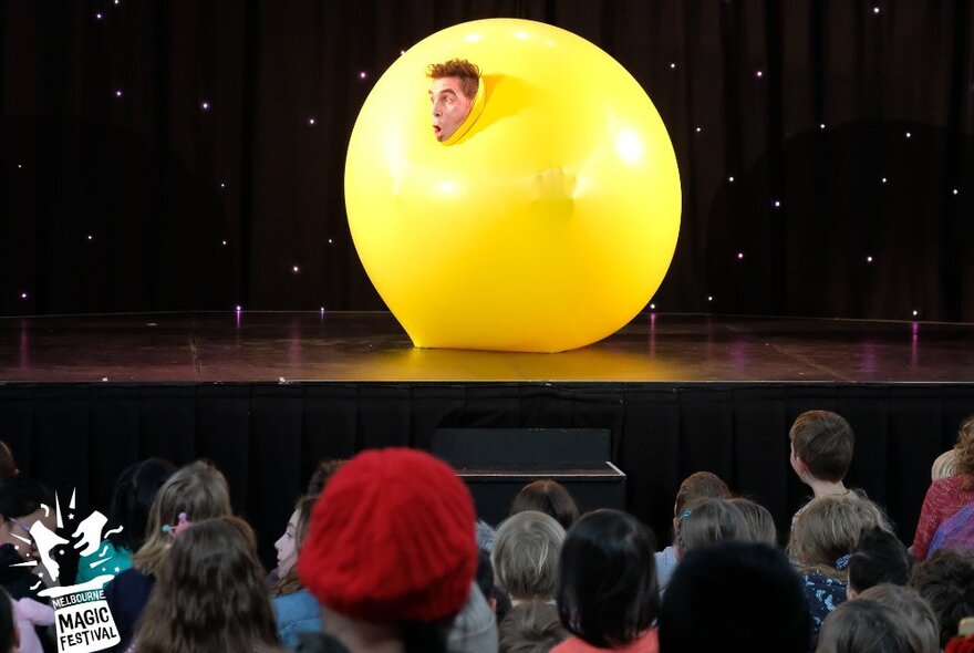The Quizzical Mr Jeff on stage performing inside a large yellow balloon. 