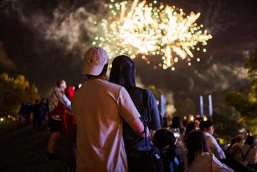 People silhouetted watching the nighttime fireworks display on the banks of Melbourne's Yarra River.