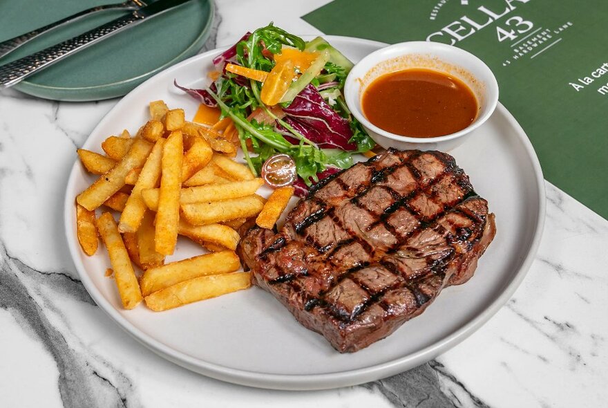 A steak, chips and green salad served on a white plate on a restaurant table. 