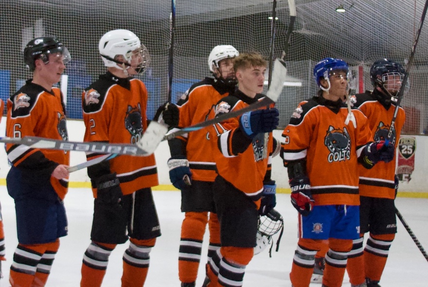 Players from the Melbourne Mustangs ice hockey team wearing their orange and black jerseys during an Australian ice hockey league match on an ice rink.