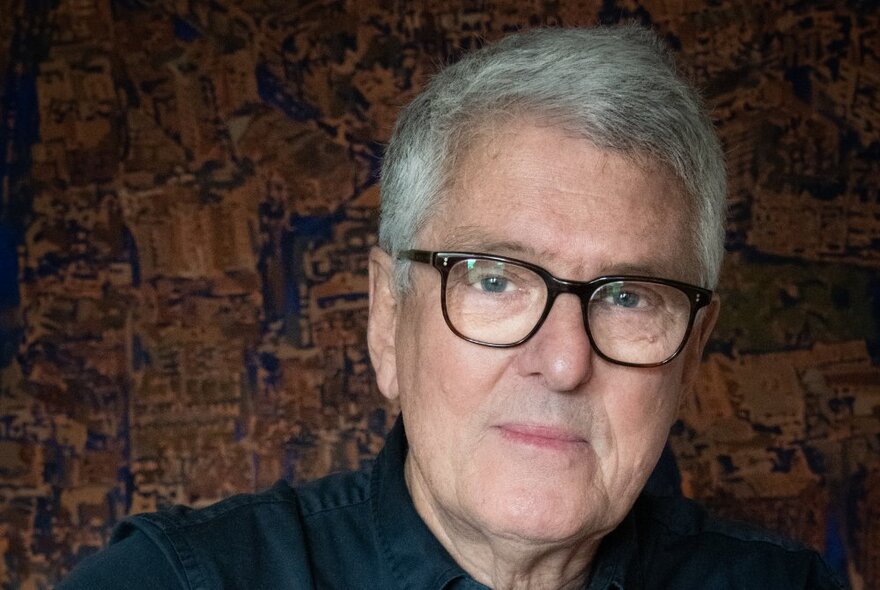 The author David Marr, a man with silver grey hair wearing glasses and with a wry smile, looking directly at the viewer.