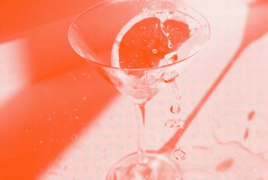 An image of a cocktail glass with wedge of fruit with an orange monochrome filter.