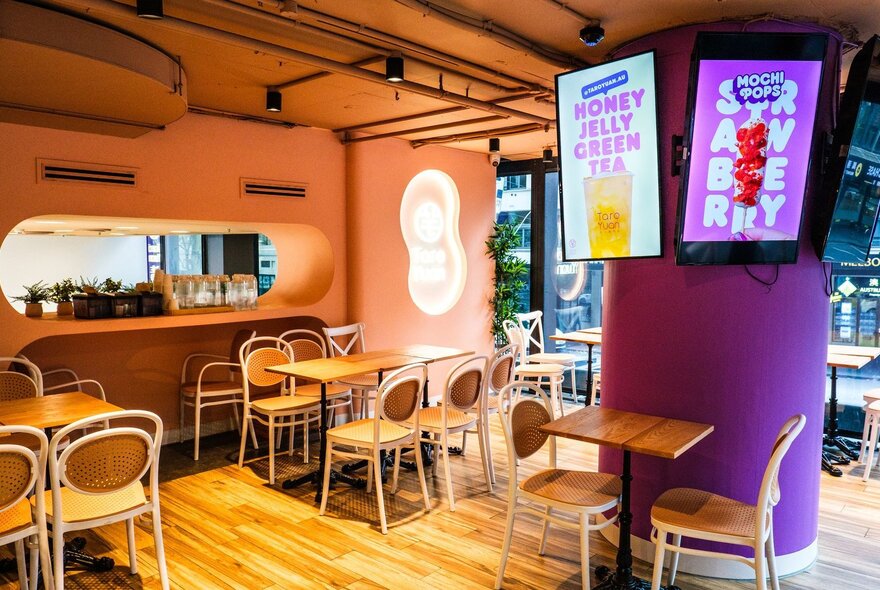 The interior of Taro Yuan in Melbourne with empty chairs and tables and a purple support column with two video screens advertising products. 