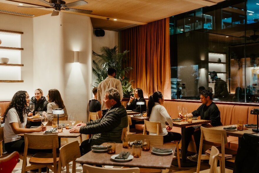 Patrons seated at tables, eating and drinking in inside a restaurant.