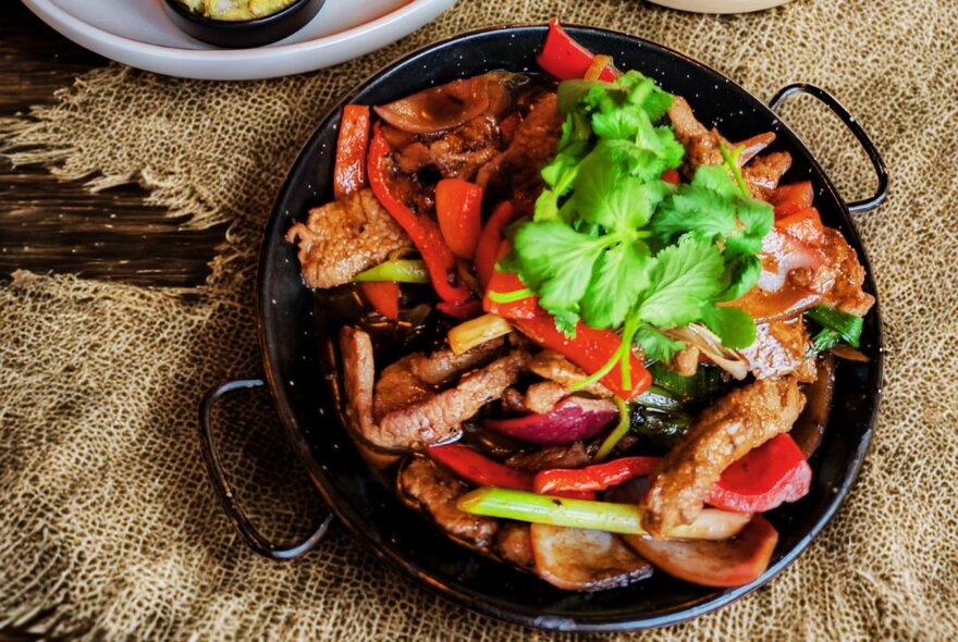Looking down at a dish of sliced beef and vegetables served in a cast iron pan, resting on a table.