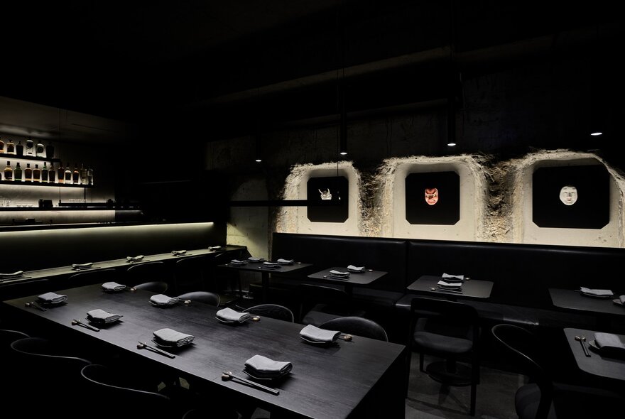 Black tables set for dinner in a black room with featuring lighting. 