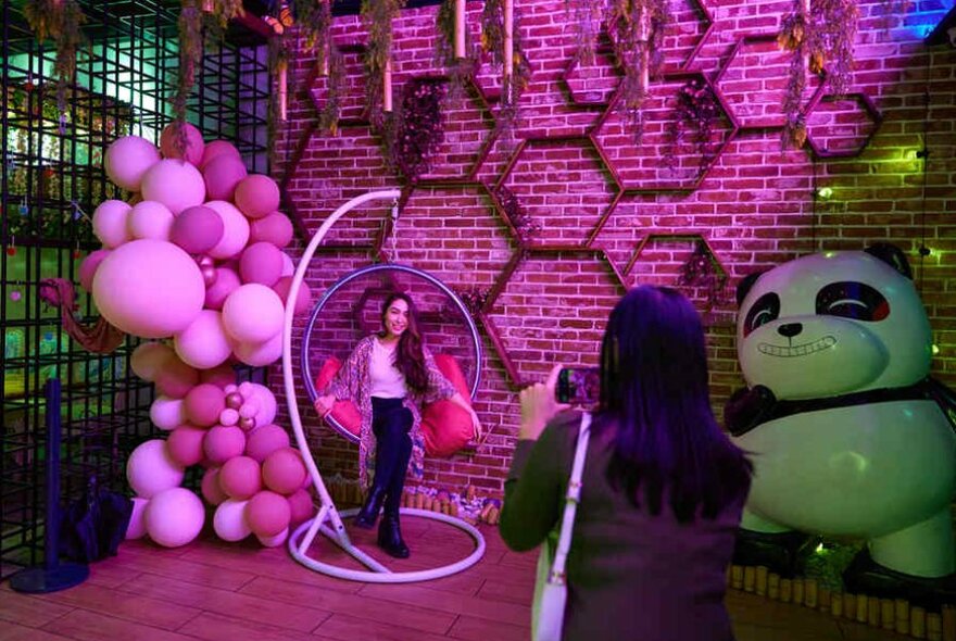 A woman sitting in a hanging chair next to a large panda figure.