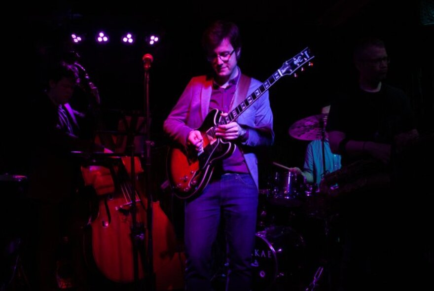 A man playing an electric guitar on a small stage with other band members in the background.