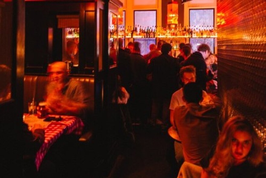 Dimly lit room at the Toff in Town showing people seated at tables eating, waiting at the bar or blurred as they are in motion.