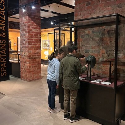 Two primary school aged children looking at objects in a glass display case at an exhibition at the Shrine of Remembrance.