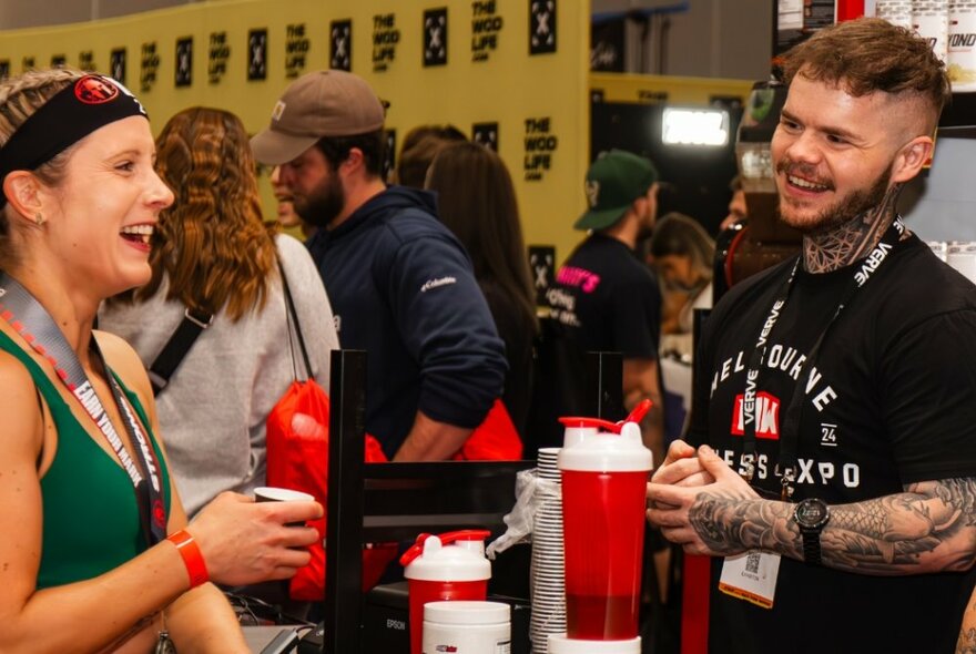 People interacting and sampling products at a stall at a fitness expo.