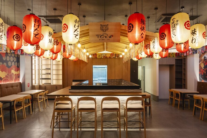 Dining room with overhead lanterns and tables surrounding a central cooking area.