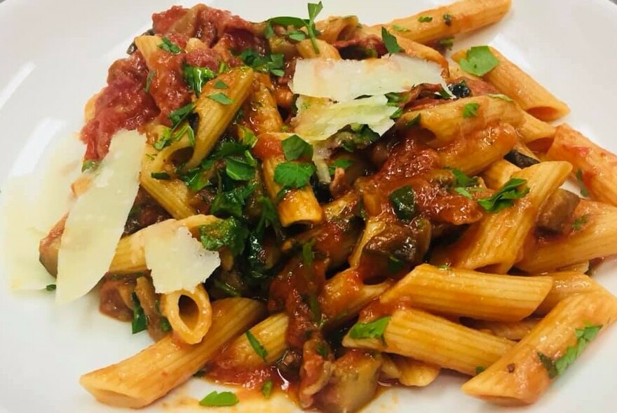 Plate of tomato penne topped with shaved parmesan and parsley.