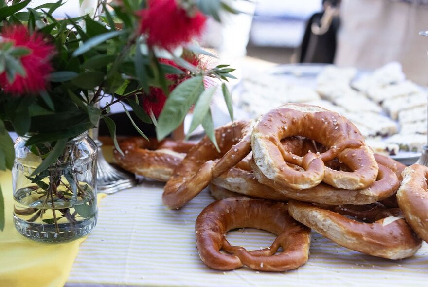 Pretzels placed casually on a table next to a vase of Bottle Brush. 