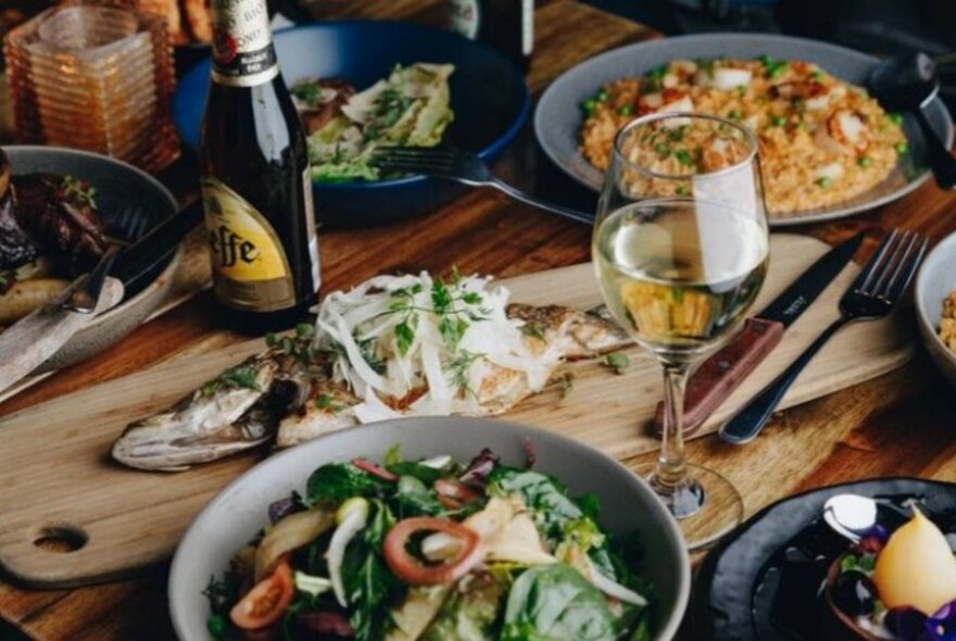 Pizza, a bowl of salad and a whole fish on a board.