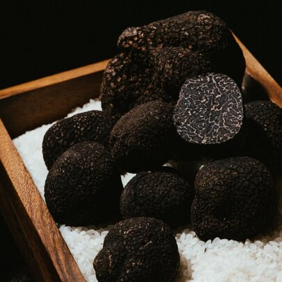 Black truffles resting on white rice grains, in a wooden box.