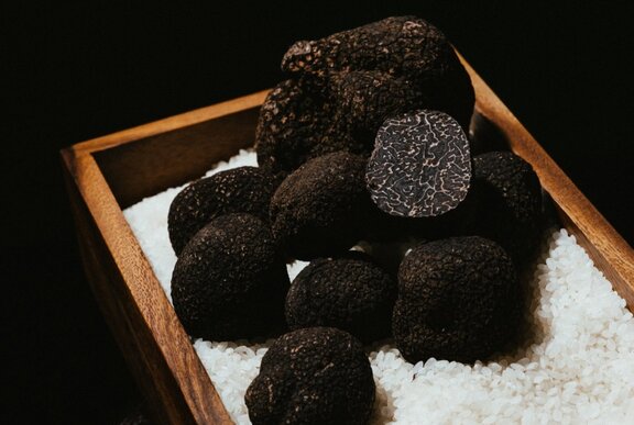 Black truffles resting on white rice grains, in a wooden box.