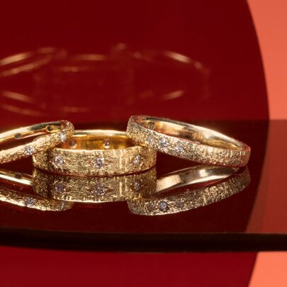Three gold rings inlaid with jewels on a dark reflective tabletop.