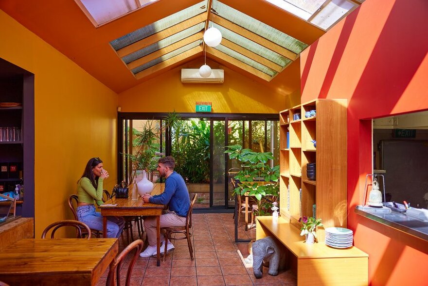 A couple dining in a restaurant with high ceilings  and orange walls.