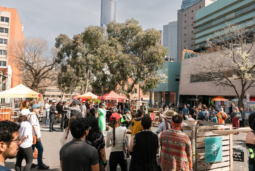 A crowd of people at an outdoor event with market stalls.