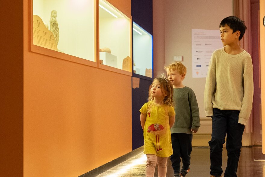 Children walking past exhibition display cases in a museum.