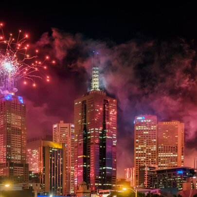 New Year's Eve red and pink fireworks lighting up the skyline of Melbourne against a dark sky.