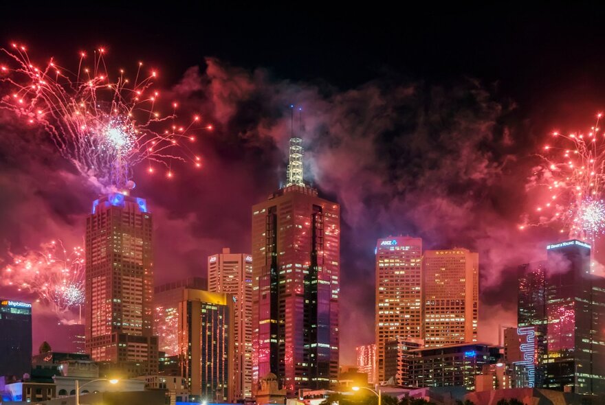 New Year's Eve red and pink fireworks lighting up the skyline of Melbourne against a dark sky.