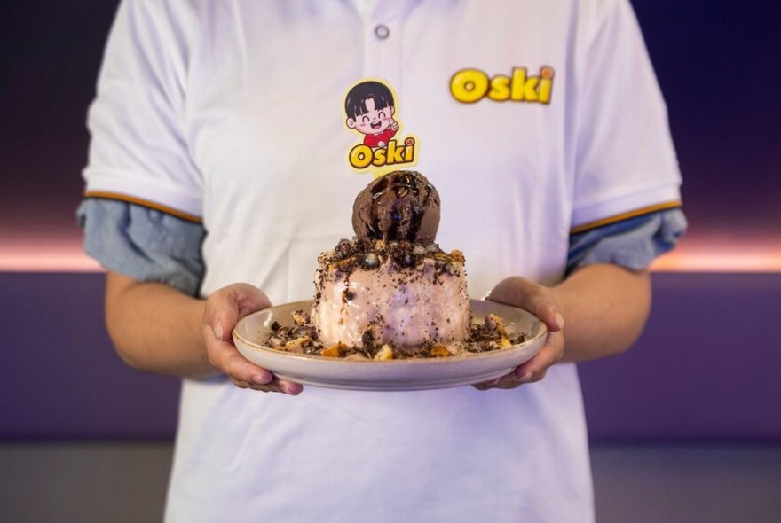 Hands holding a plate of dessert with a staff t-shirt visible. 