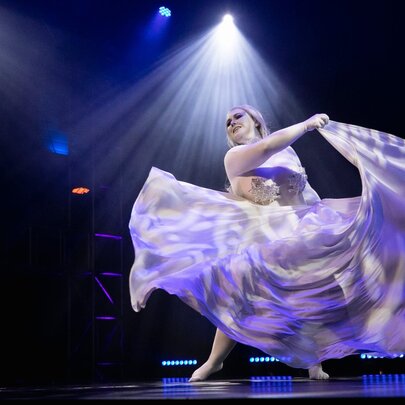 A burlesque dancer on stage twirling so their large skirt is flowing around them. 