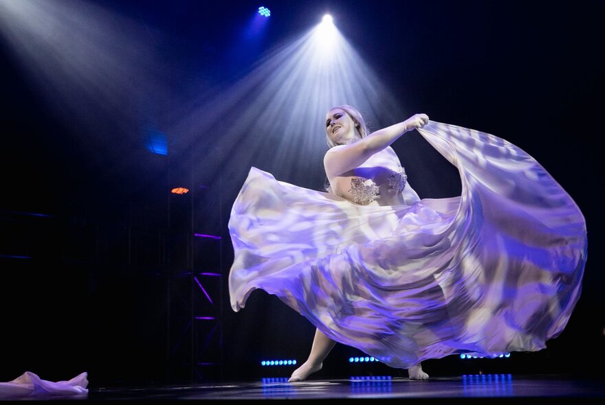 A burlesque dancer on stage twirling so their large skirt is flowing around them. 