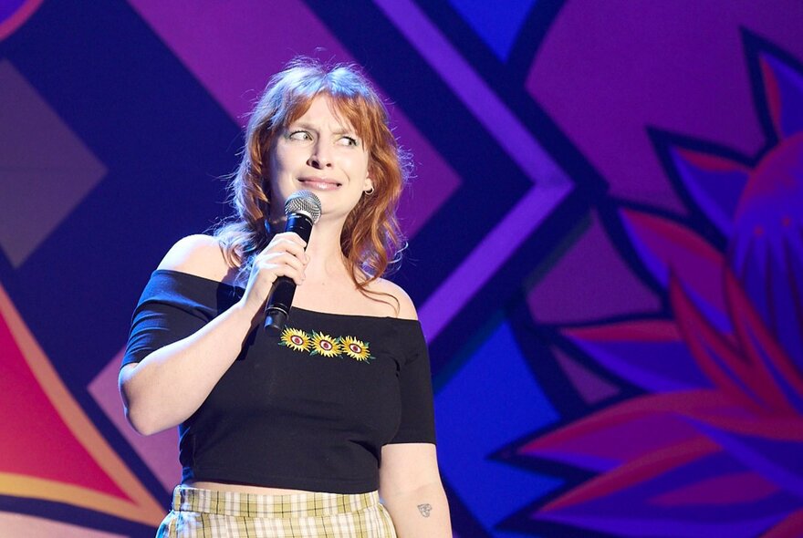 Performer Robyn Reynolds on stage, holding a microphone in her hands, grimacing.