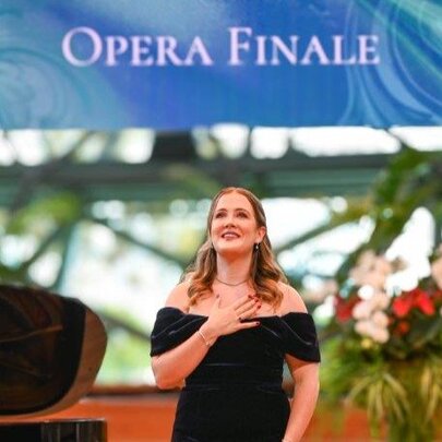 A young woman in a black, off-shoulder evening gown underneath an OPEA FINALE sign. 