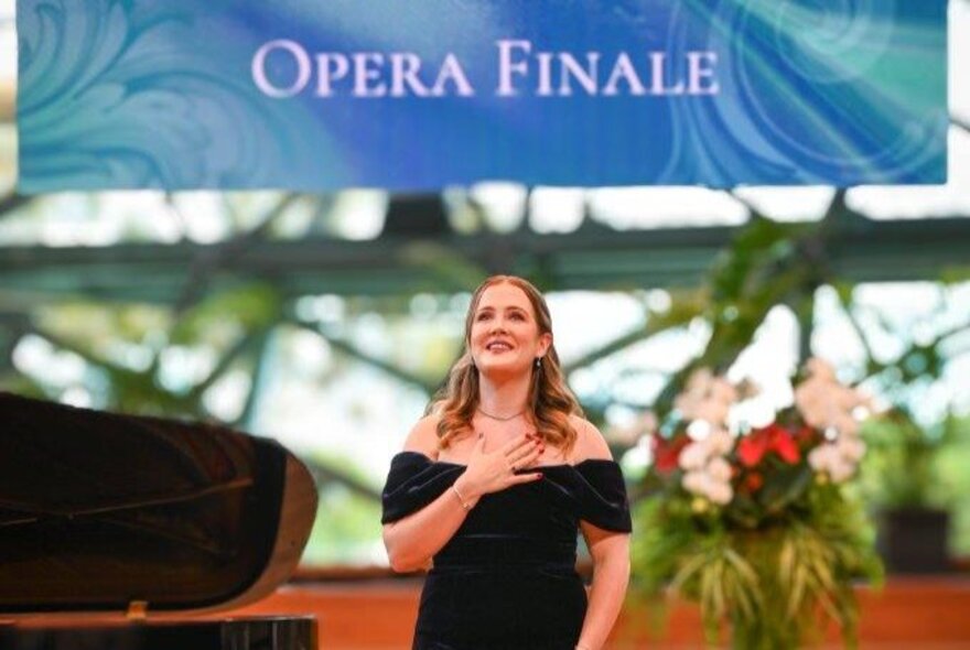 A young woman in a black, off-shoulder evening gown underneath an OPEA FINALE sign. 